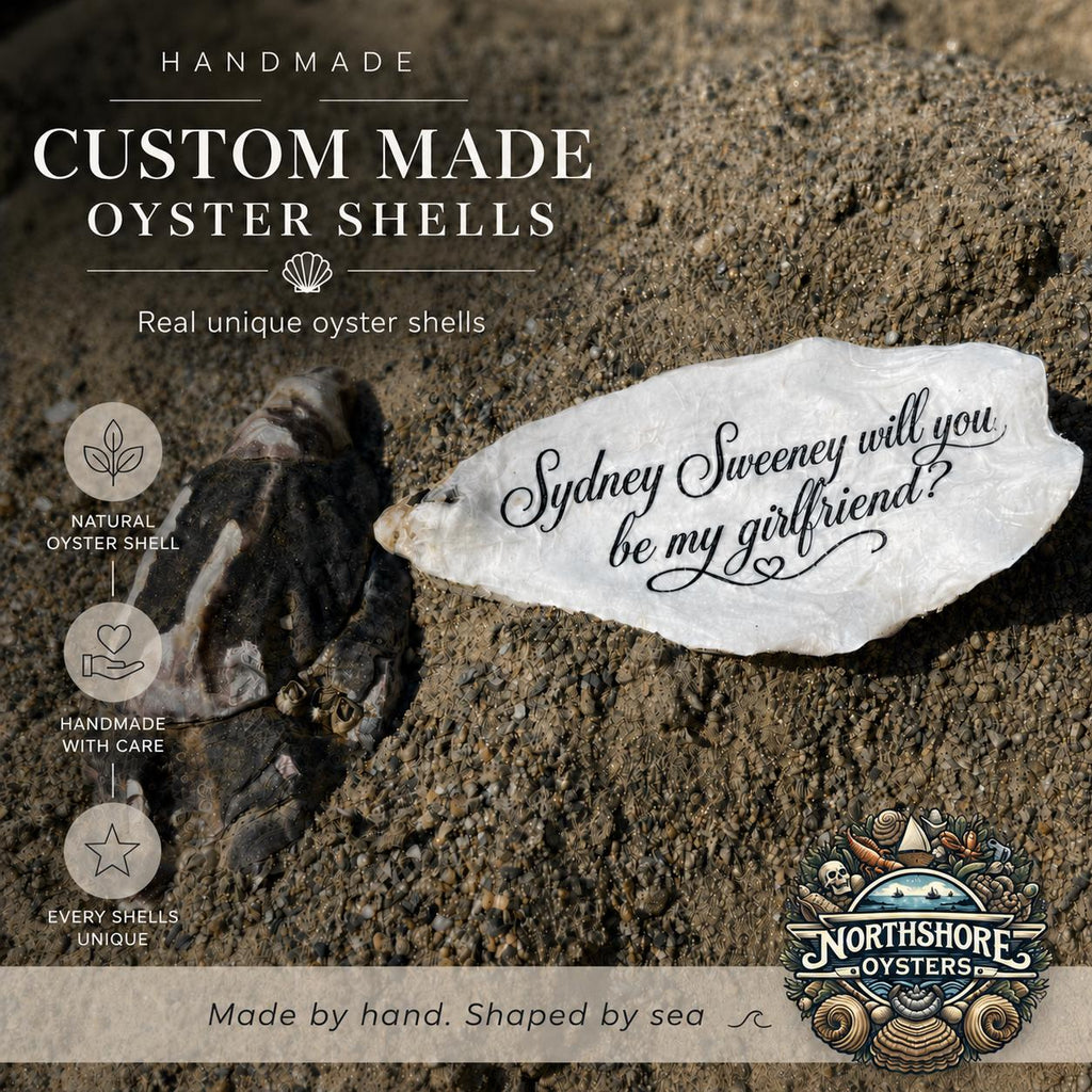A custom engraved oyster shell with the phrase 'will you be my girlfriend?' displayed on a sandy beach next to a natural dark oyster shell. The image features promotional text highlighting handmade and custom-made oyster shells.